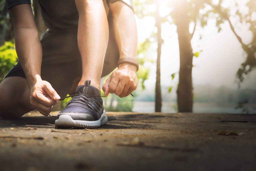 Homem Amarrando o Tenis pronto para correr num parque com pulseira